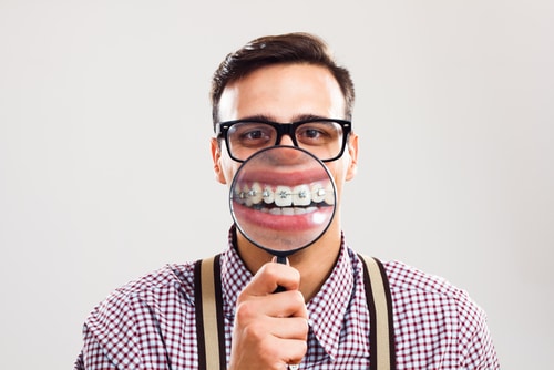 Man in braces with orthodontic braces holding magnifying glass