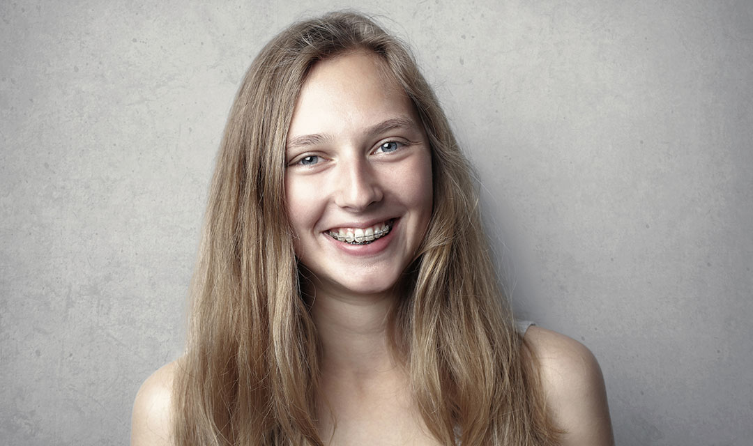 Young female presenting person with long blond hair smiling with braces